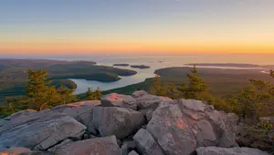 Sunset view from Beech Mountain Acadia National Park showing rocky summit foreground and tranquil ocean bays dotted with forested islands