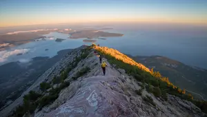 Hikers ascending the Cadillac North Ridge Trail in Acadia National Park at sunrise, overlooking Frenchman Bay and the coastal islands below.